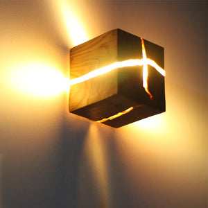 The Wood Cube Wall Light, constructed with a natural wood grain, showcases glowing slits that emit warm light rays, embracing a contemporary design.