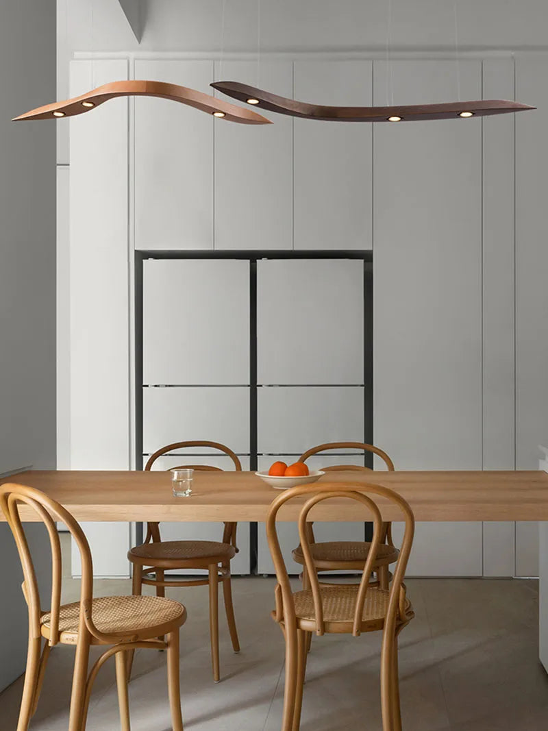 Minimalist kitchen with a wooden dining table, four cane chairs, a glass of water, a plate of oranges, and two Spiral Wood Pendant Lights overhead for an organic modern touch.
