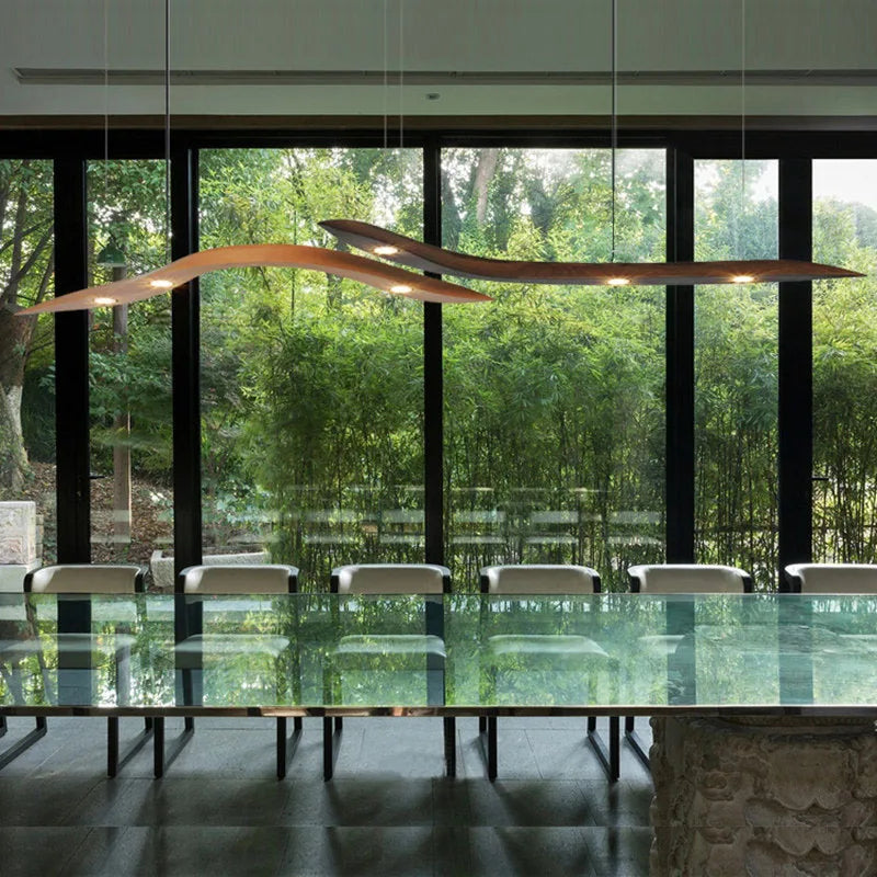 A modern dining room features a glass table, white chairs, the Spiral Wood Pendant Light, and large windows offering views of green bamboo outside.