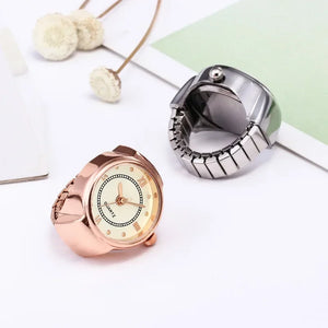 Two Eternal Ring Watches, one rose gold and one silver, are displayed on a white surface beside dried flowers and paper.