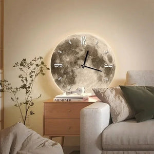 A round Moon Wall Clock with a glow-in-the-dark lunar surface texture and minimalist numbering is mounted above a wooden nightstand beside a beige sofa.