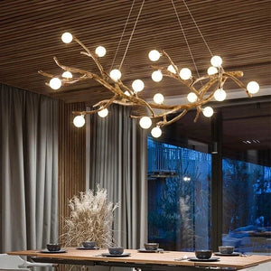 A modern dining room flaunts an organic lighting style with the Branch Pendant Light, featuring glass orb shades. The wooden ceiling and large windows with gray curtains frame a table for four, set with dark dishware.