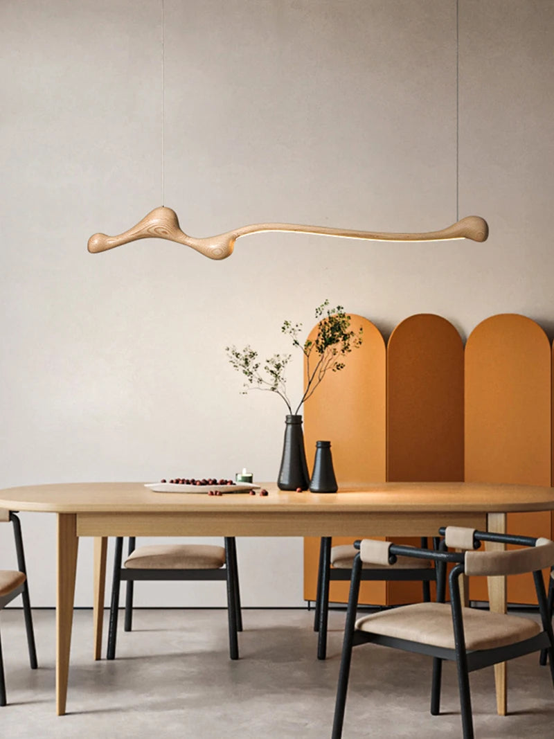 A modern dining room with a light wood table, four chairs, a Nordic minimalism touch from the Tideform Biomorphic Pendant Light in ash wood, and an orange room divider set against a neutral wall.