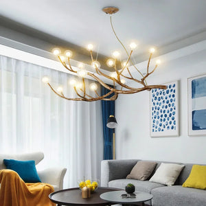 A contemporary living room showcases a Branch Pendant Light with glass orb shades, complemented by a gray sofa, yellow throw, a side chair, a floor lamp, and abstract wall art.