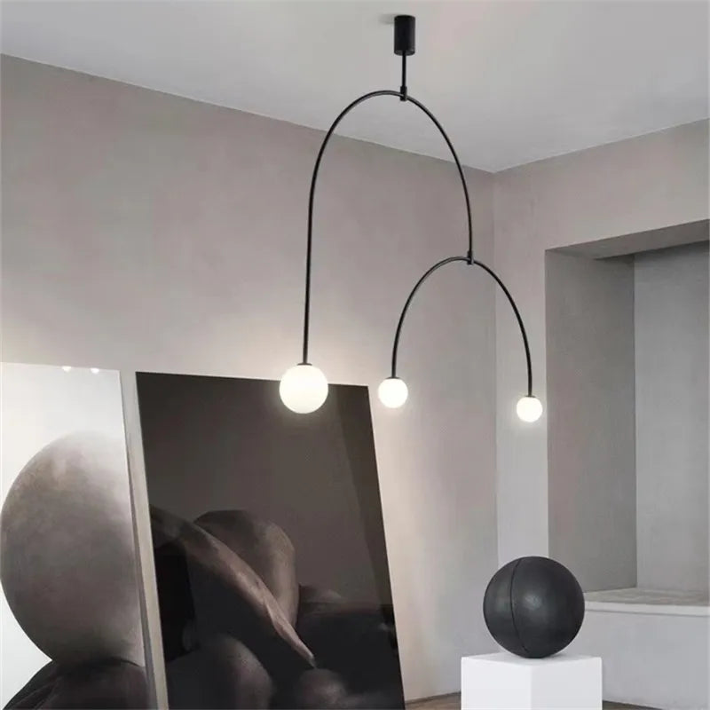 A modern interior features sculptural lighting with a Minimalist Line Light pendant, abstract art pieces leaning on a wall, and a round black sculpture on a white pedestal.