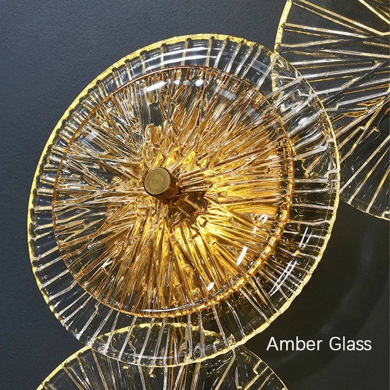 Close-up of the Amber Deco Wall Sconce featuring a circular amber glass disc with radial patterns, mounted on a dark wall. Text in the corner reads "Amber Deco Wall Sconce.