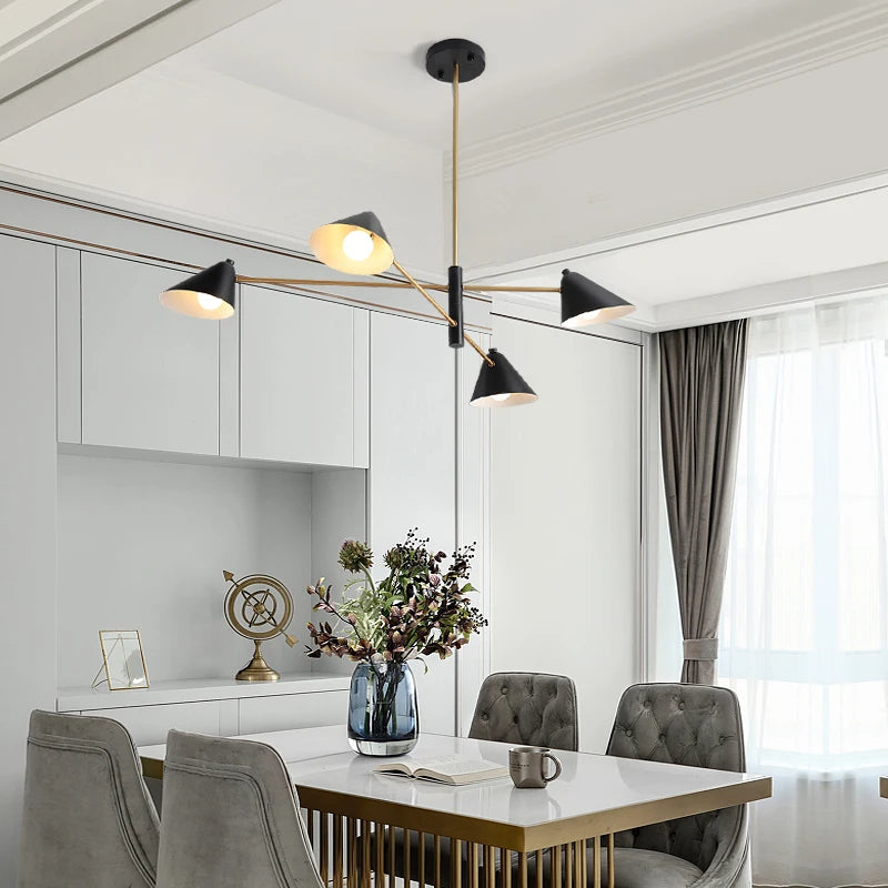 A modern dining room showcases a minimalist Multi-Arm Ceiling Light with black and gold pendant accents. It includes four chairs, a vase with flowers on the table, and neutral tones. A large window with curtains lets natural light enhance the lighting.