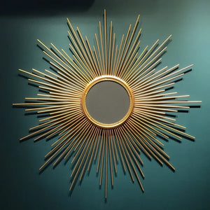 A Luxe Sunray Wall Mirror with a gold sunburst frame is mounted on a teal wall, creating a striking statement feature in the interior design.