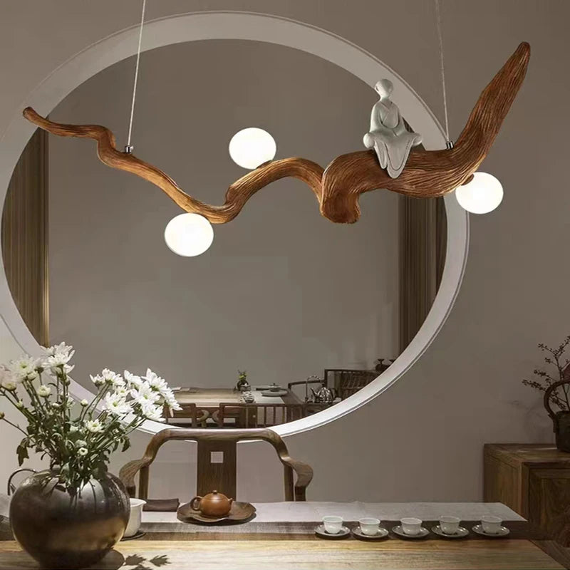 A room featuring a circular mirror, natural wood furniture, and the Zen-Inspired Wooden Pendant Light resembling a branch with a small figurine creates a serene Zen aesthetic.