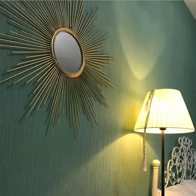 A Luxe Sunray Wall Mirror hangs on a green textured wall above a lit floor lamp with a cream shade, bringing statement interior style next to a white metal bed frame.