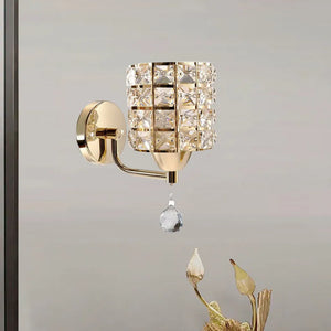 The Luxury Cylinder Wall Light, with its crystal-covered shade and hanging drop, adds an elegant touch of luxury lighting above dried flowers on a plain light-colored wall.