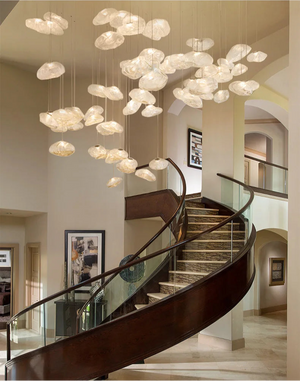A modern spiral staircase with glass railing stands beneath a ceiling installation featuring Luxe Cloud Glass Pendant Lights—sculptural, translucent disc-shaped lamps—in a spacious, elegant interior.