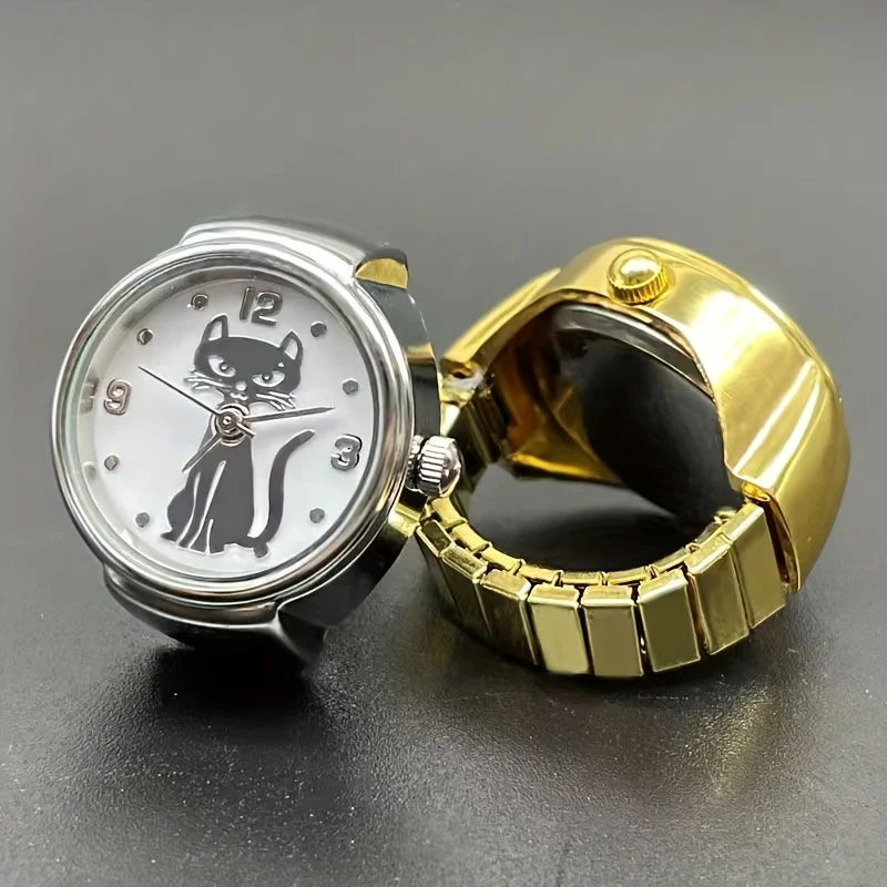 The Cat Ring Watch features a gold metal band and a white face with a black cat illustration at the center, highlighting feline elegance. Shown open on a simple dark surface, this unique timepiece is both stylish and charming.