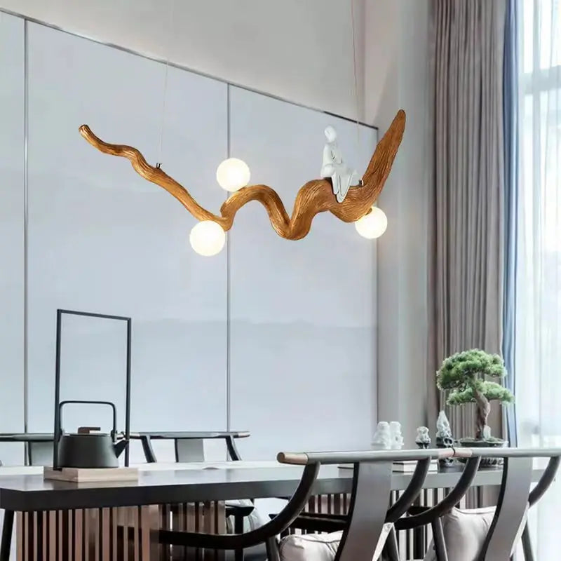 A modern dining room showcases the Zen-Inspired Wooden Pendant Light, a wooden branch chandelier with round lights, and a small white decorative figure elegantly above the table for a Zen aesthetic.