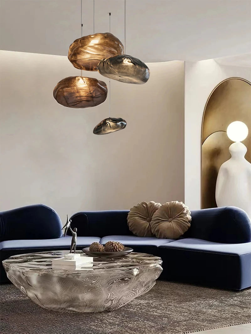 Modern living room with a curved navy sofa, textured pillows, abstract glass coffee table, Luxe Cloud Glass Pendant Light, and a sculptural lamp in front of an arched wall feature.