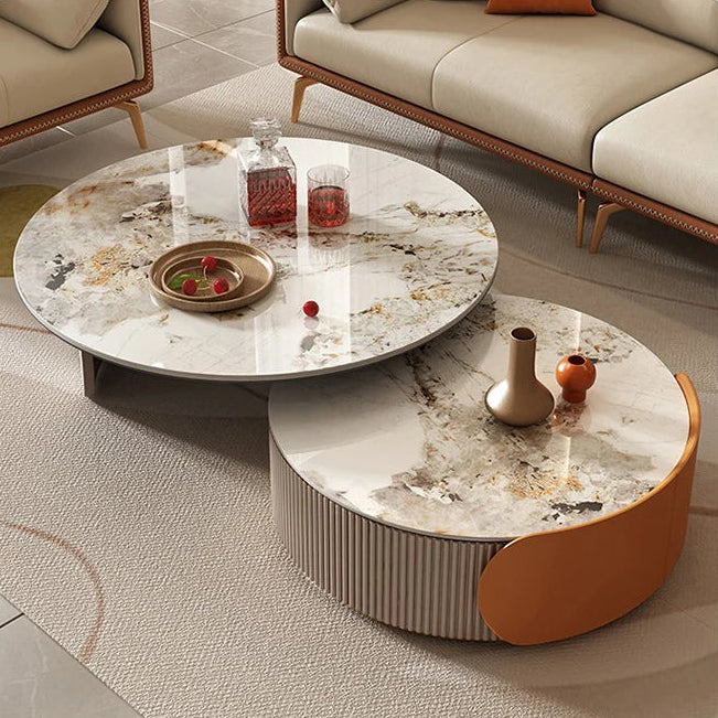 A Luxe Round Coffee Table with drinks, fruit, and decorative vases stands in a modern living room featuring beige sofas and a textured carpet.