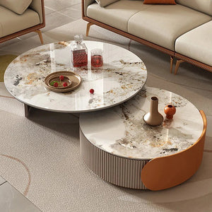 A Luxe Round Coffee Table with drinks, fruit, and decorative vases stands in a modern living room featuring beige sofas and a textured carpet.