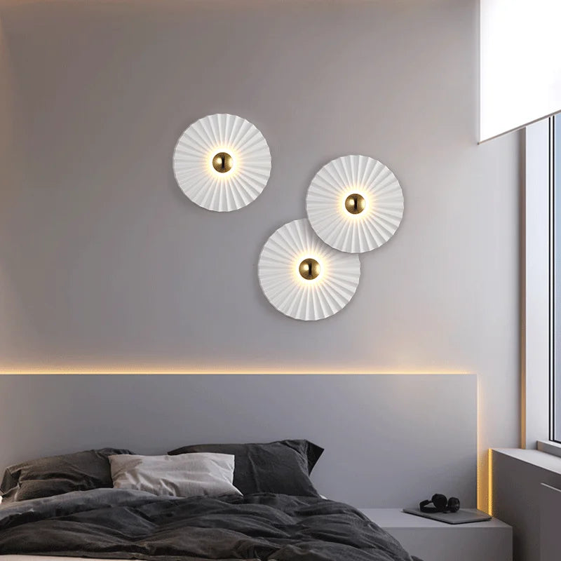 A modern bedroom with a gray bed, minimal bedding, and three Origami Circle Wall Lights above the headboard; a window on the right fills the space with natural light.