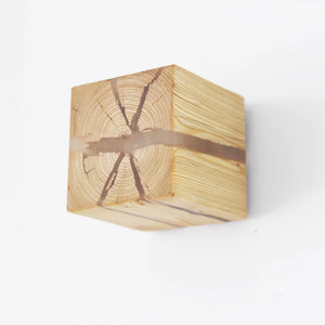 A close-up of the Wood Cube Wall Light showcases its natural wood grain and characteristic crack, embodying contemporary design against a white background.