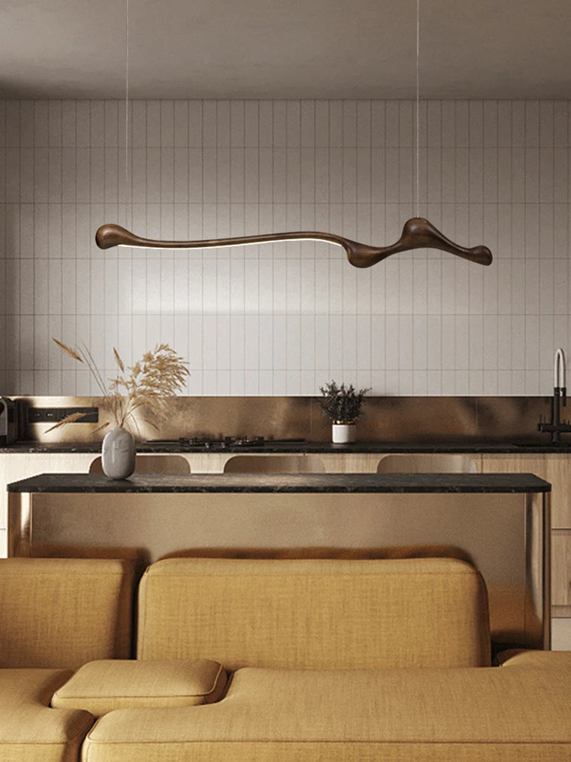 Modern kitchen with minimalist design, featuring the Tideform Biomorphic Pendant Light above a dark countertop and beige cabinetry, complemented by tan seating in the foreground.
