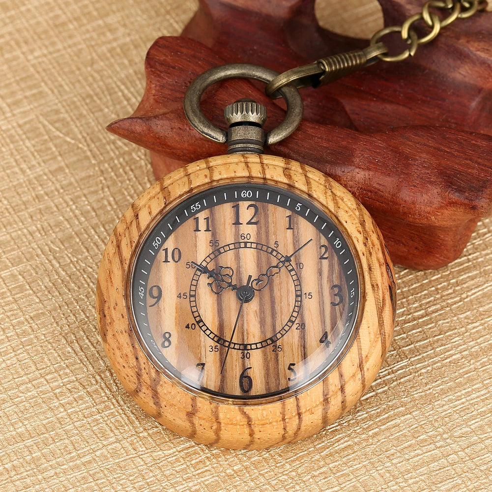 The Wooden Pocket Watch features black numerals and ornate hands on wood, attached to a brass chain, and rests on a beige textured surface beside a carved wooden object, highlighting its vintage-inspired charm.
