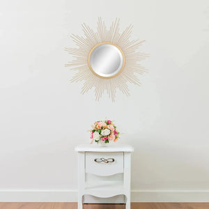 A Luxe Sunray Wall Mirror hangs above a small white table with a drawer, topped with a flower arrangement, making a statement against the plain white wall.
