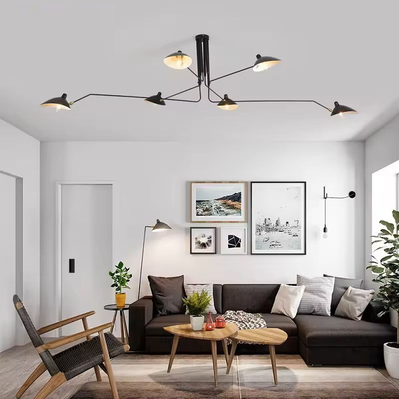 A modern living room features a black sectional sofa, small wooden tables, plants, and wall art. The Sleek Industrial Pendant Light and a black floor lamp illuminate the space with elegance through brass connection points.