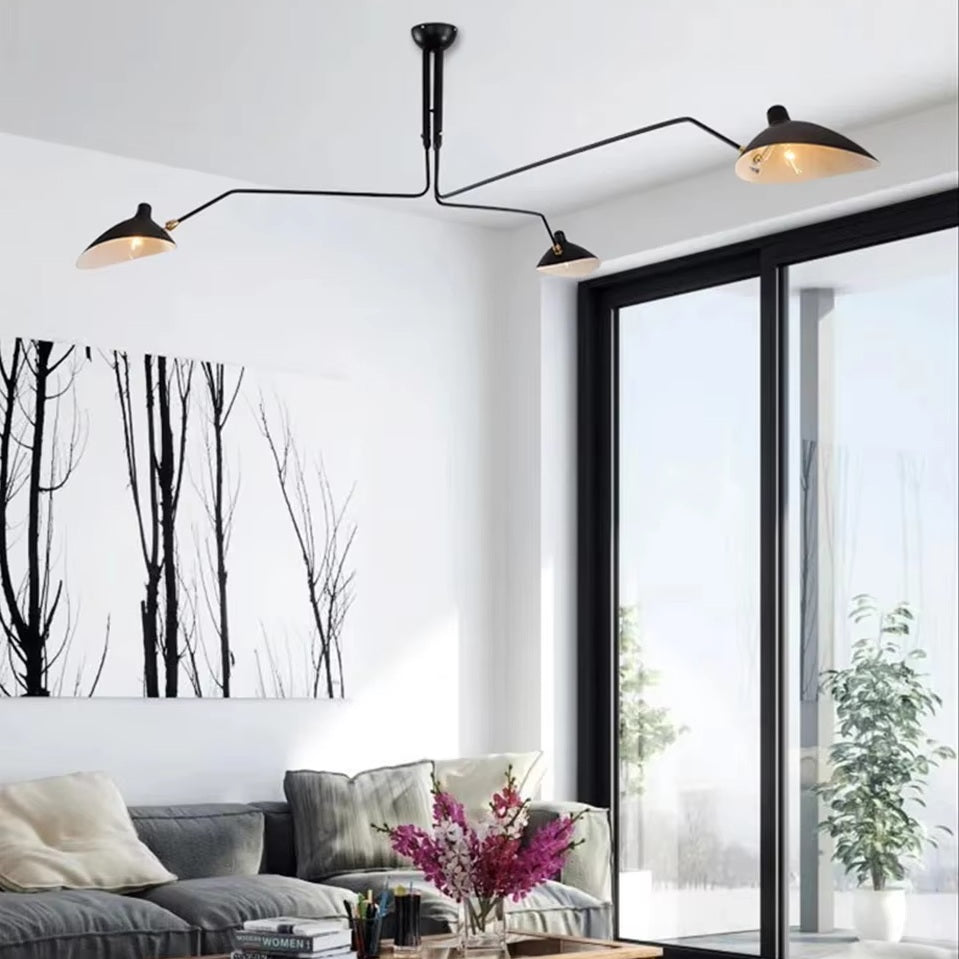 A modern living room features a gray sofa, abstract tree artwork, and the Sleek Industrial Pendant Light with brass accents. Large glass doors reveal plants outside.