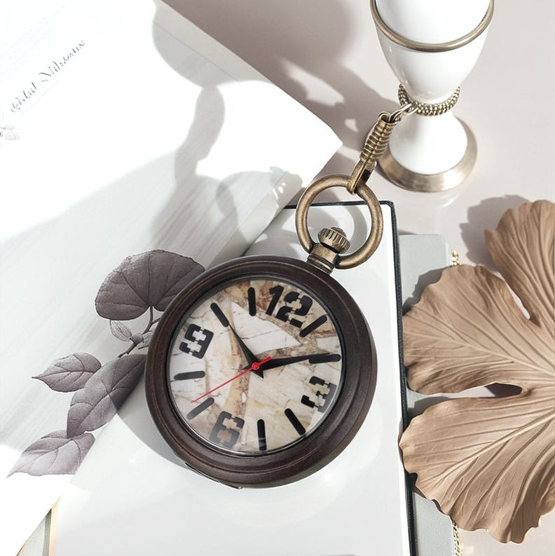A Vintage Style Pocket Watch with a marble-patterned face is displayed on a white surface beside decorative leaves, a candlestick, and an open notebook—highlighting the elegance of marble face timepieces.