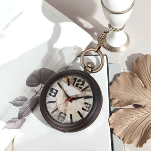 A Vintage Style Pocket Watch with a marble-patterned face is displayed on a white surface beside decorative leaves, a candlestick, and an open notebook—highlighting the elegance of marble face timepieces.