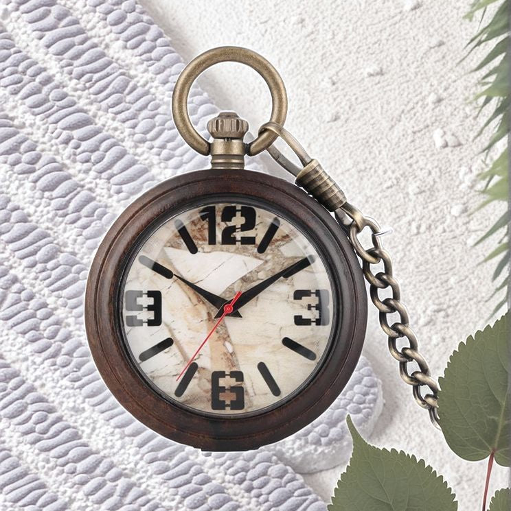 The Vintage Style Pocket Watch, featuring a marble-patterned face and bold black numerals, rests on a textured white surface beside green leaves, capturing the timeless elegance of classic timepieces.