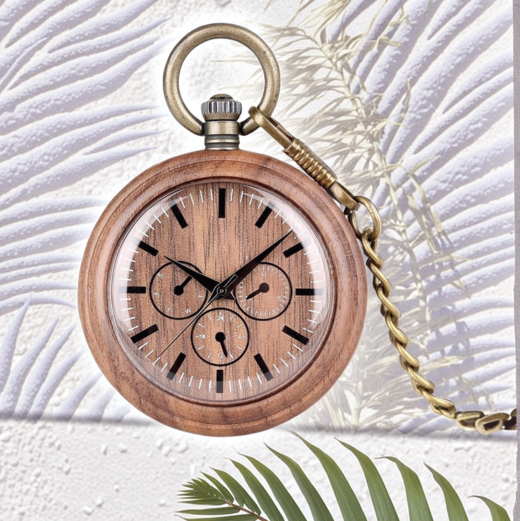 The Handmade Wood Pocket Watch with a brass chain rests on a textured white surface, surrounded by dancing palm leaf shadows and a green palm frond in the foreground.