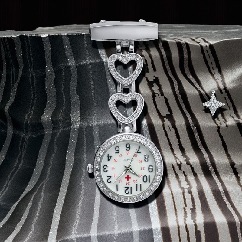 The Luxe Fob Pocket Watch with heart-shaped links and rhinestones rests on a striped fabric background, accented by a small star-shaped brooch nearby.