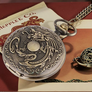 A Dragon Pocket Watch with an ornate, engraved design rests on paper marked "HEPPLE CO.", while another vintage timepiece is partially visible nearby.