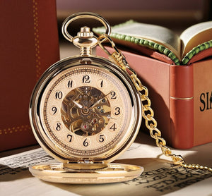 The Premium Golden Pocket Watch, featuring an open lid and skeleton dial, rests on papers with its golden chain elegantly draped; blurred books provide the background.
