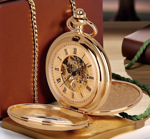 The Golden Roman Pocket Watch, featuring a gold skeleton movement and Roman numerals, sits open by a brown box and green cord, showcasing its vintage mechanical charm.