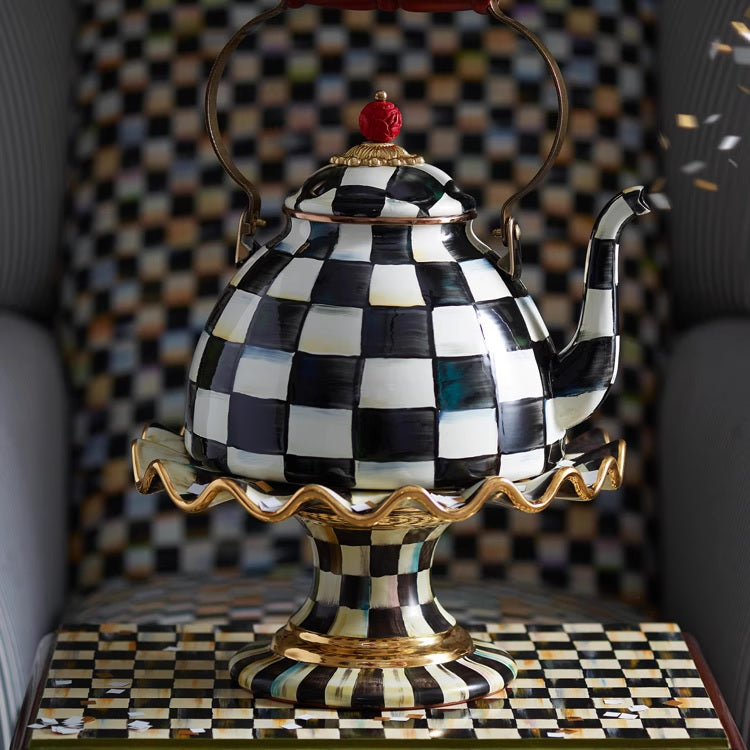 The Vintage Black and White Kettle, featuring a bold checkered pattern and gold accents, sits on a matching pedestal. Both the background and surface showcase the striking black-and-white checkerboard design.