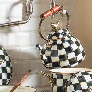 The Vintage Black and White Kettle, featuring a sparrow-shaped knob, rests above matching cookware in a kitchen with white tile backsplash and exposed metal pipes.