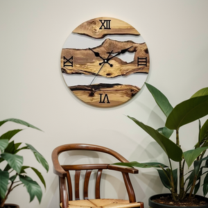 A Wood Circular Wall Clock with Roman numerals hangs on the wall above a wooden chair, exuding an organic style. Nearby, two potted plants enhance the natural appeal, creating a serene ambiance.