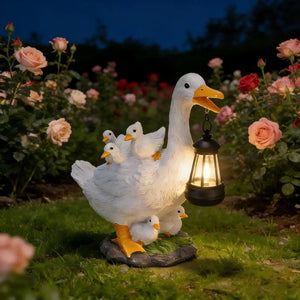 A Solar Duck Lamp stands in the garden among pink and red roses, holding a glowing solar-powered lantern and surrounded by gosling figures at night.