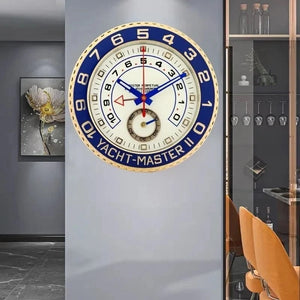 The Rolexia Wall Clock embodies modern luxury, echoing the elegance of a Rolex Yacht-Master. It enhances interior design as an exquisite piece, standing out against gray walls and vibrant orange chairs.