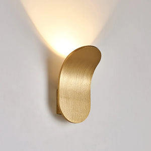 The Curved Wall Light, a Nordic-inspired wall lamp featuring a brushed metal design in gold, emits light upwards and is mounted on a white wall. Perfect for living spaces seeking modern light fixtures that seamlessly blend elegance and functionality.