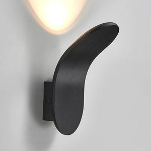 A Curved Wall Light in matte black with a sculptural design casts soft light, enhancing modern living spaces.