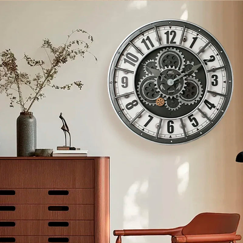 An Industrial Gearworks Wall Clock with exposed gears hangs above a wooden dresser topped with a vase of dried branches, books, and a modern sculpture.