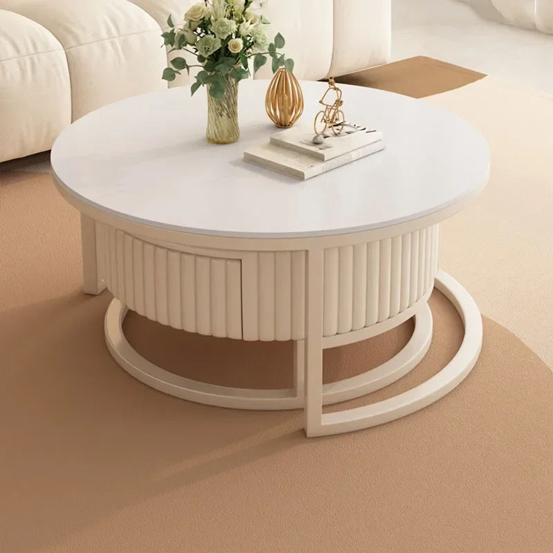 The Luxury Round Coffee Table Set features a minimalist marble-look design and is styled with a decorative vase, books, and ornament on top, all placed on a beige carpet in a modern living room.