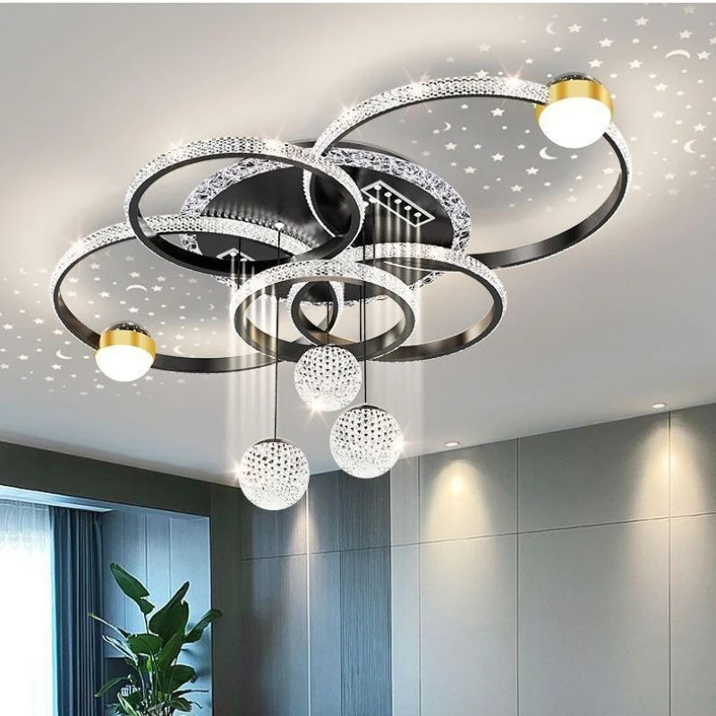 The Elegant Multi-Ring Ceiling Light features circular LED rings and crystal spheres that project star patterns onto the ceiling, enhancing a contemporary room with gray walls and a tall green plant.