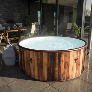 A round Outdoor Spa Hot Tub with bubbling water sits on a tiled patio near outdoor furniture and plants, positioned outside a modern house with large glass doors. This inviting Outdoor Spa Hot Tub creates the perfect backyard oasis, seamlessly blending relaxation and style for an exceptional outdoor spa experience.