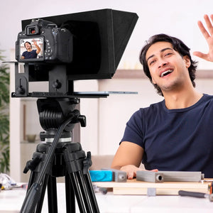 A person sits behind a camera mounted on a tripod, utilizing the Universal Portable Teleprompter, while speaking and gesturing energetically.