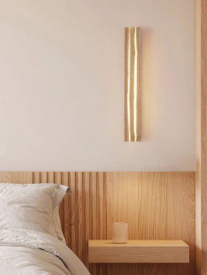 A minimalist bedroom showcases a wooden aesthetic with a Rectangle Wood Wall Light, a wooden headboard, and a floating nightstand with a glass of water.