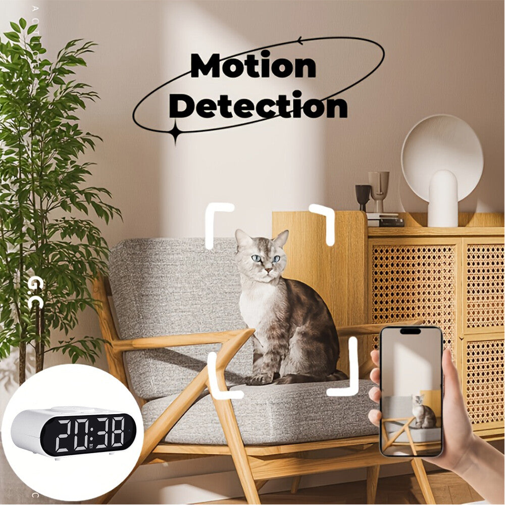 A gray cat sits on a chair as a hand holds a smartphone displaying the Digital Clock Charger SpyCam’s live WiFi feed of the cat; "Motion Detection" and a digital clock appear on screen.
